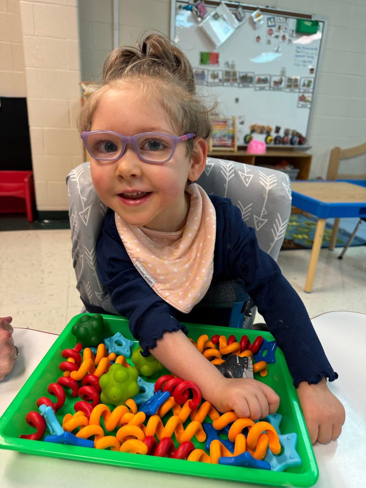 Gracie wearing purple glasses and playing with colorful toys at a classroom table.