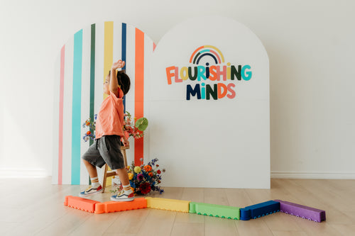 A child on colorful balance blocks in front of the Flourishing Minds logo