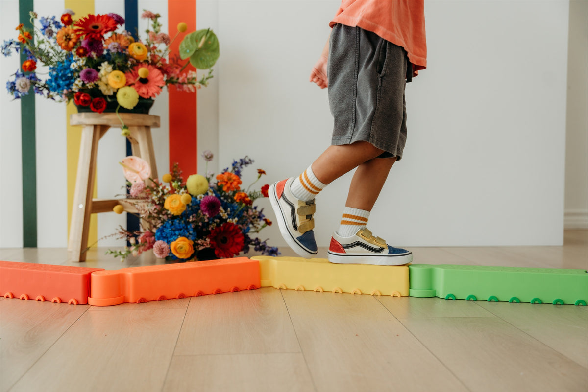 A child balancing on colorful blocks beside flower arrangements